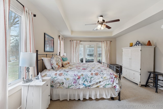 bedroom featuring a ceiling fan, access to exterior, a raised ceiling, and light carpet