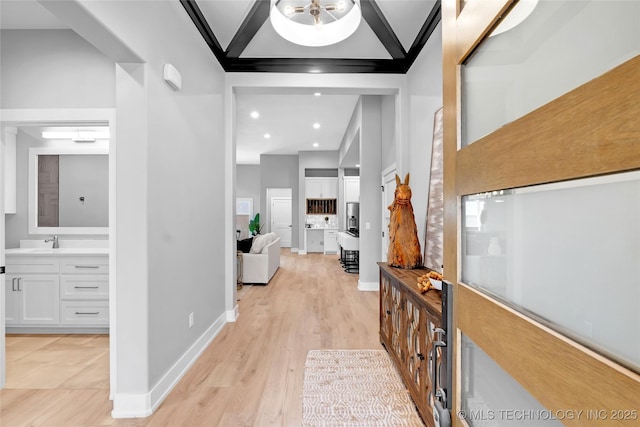 hall featuring recessed lighting, baseboards, a sink, a towering ceiling, and light wood-style floors