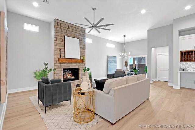 living room featuring a large fireplace, light wood-type flooring, baseboards, ceiling fan with notable chandelier, and recessed lighting