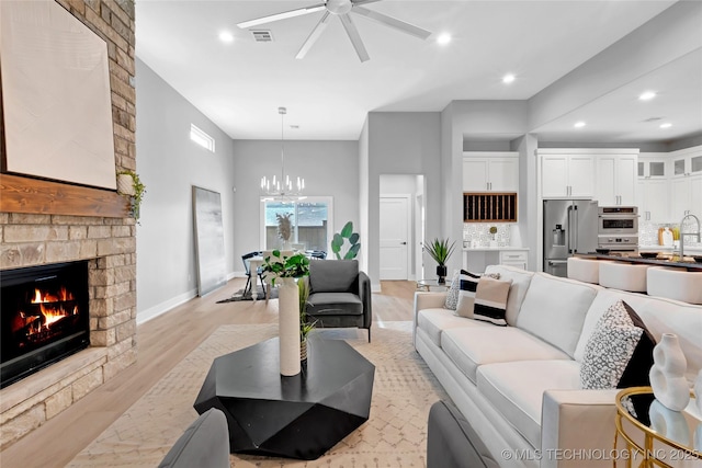 living area with a large fireplace, light wood-style flooring, baseboards, ceiling fan with notable chandelier, and recessed lighting