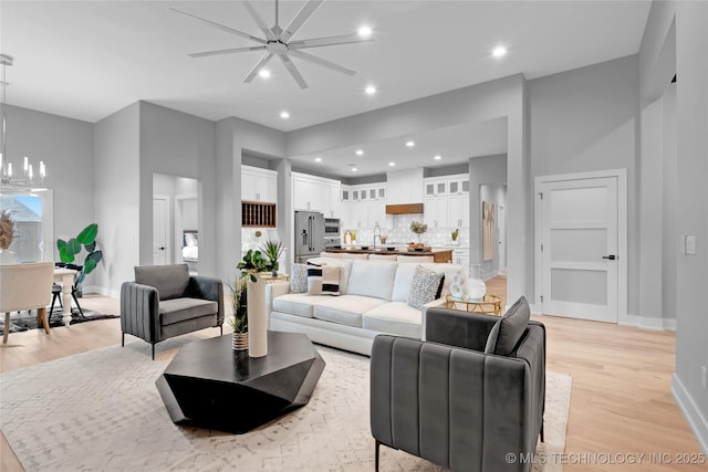 living area with ceiling fan with notable chandelier, light wood-type flooring, baseboards, and recessed lighting