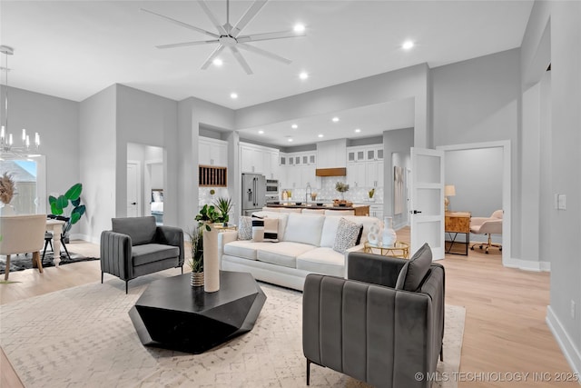 living area with light wood finished floors, ceiling fan with notable chandelier, recessed lighting, and baseboards