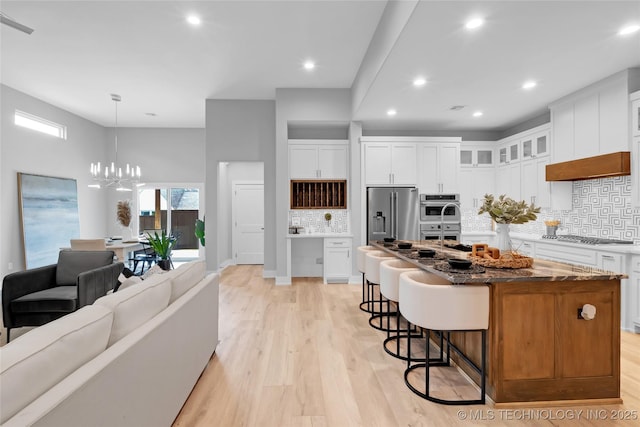 kitchen featuring light wood-style flooring, a breakfast bar, stainless steel appliances, an island with sink, and a notable chandelier