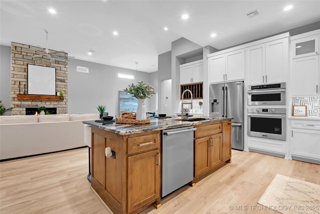 kitchen with white cabinets, light wood finished floors, a kitchen island with sink, appliances with stainless steel finishes, and a sink