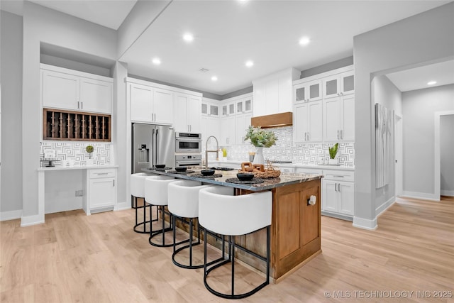kitchen with a kitchen island with sink, light wood-style flooring, a kitchen bar, and stainless steel appliances