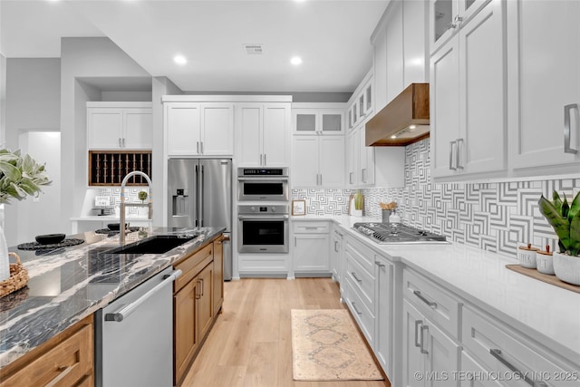 kitchen with stainless steel appliances, decorative backsplash, dark stone counters, a sink, and light wood-style floors