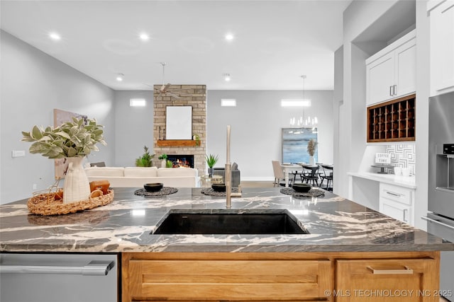kitchen with open floor plan, dark stone countertops, a sink, appliances with stainless steel finishes, and a fireplace