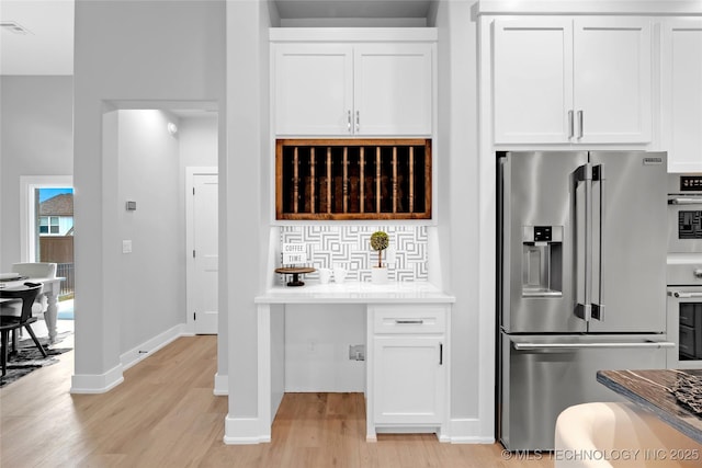 kitchen featuring light countertops, light wood-style flooring, stainless steel appliances, white cabinetry, and backsplash