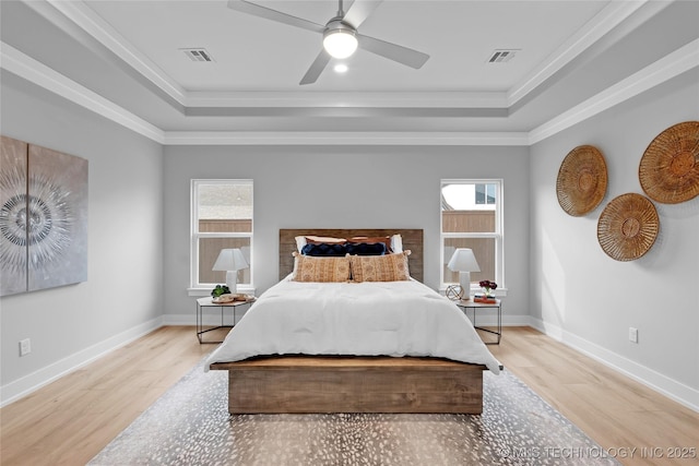 bedroom with wood finished floors, a tray ceiling, baseboards, and visible vents