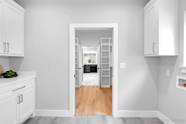 clothes washing area with baseboards, cabinet space, hookup for a washing machine, and light wood finished floors