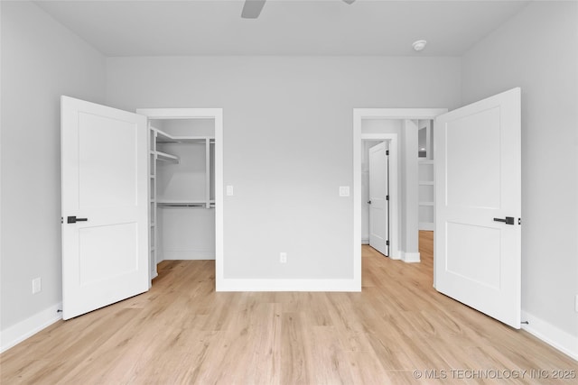 unfurnished bedroom with baseboards, light wood-style flooring, and a walk in closet