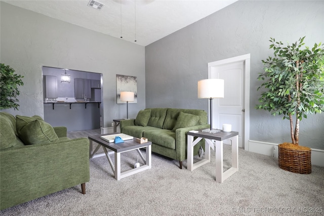 living room featuring vaulted ceiling, a textured wall, carpet floors, and visible vents