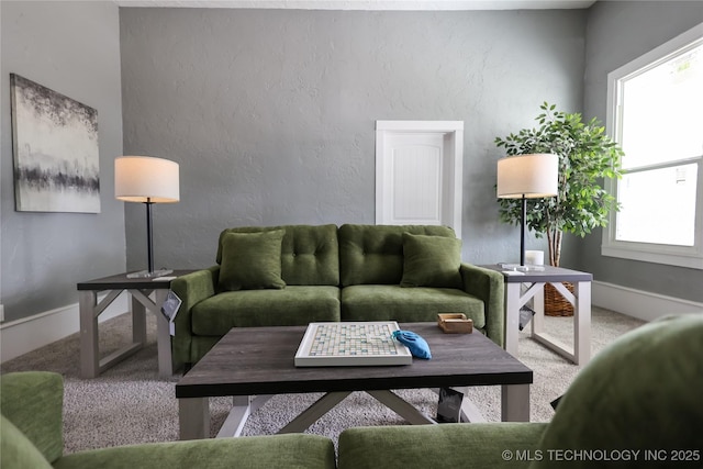 living area featuring a textured wall, carpet floors, and baseboards