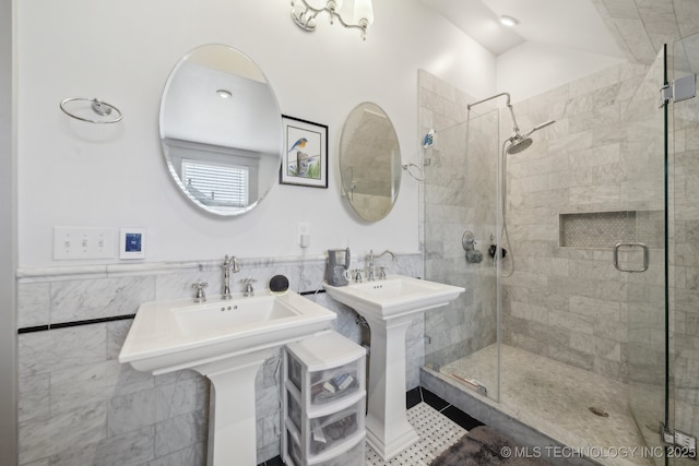 bathroom featuring dual sinks, a shower with shower door, and tile walls