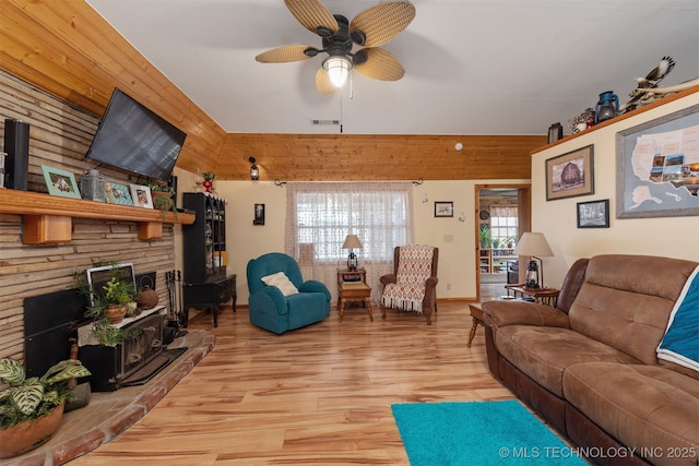 living room with visible vents, light wood-style flooring, a ceiling fan, and wood walls