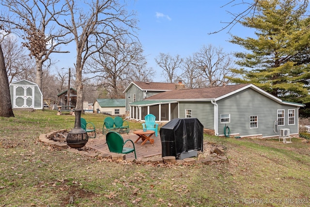 rear view of house featuring a lawn, a shed, an outdoor fire pit, a sunroom, and a chimney