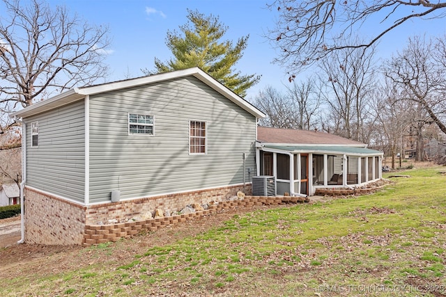 view of home's exterior with brick siding, central AC, a yard, and a sunroom