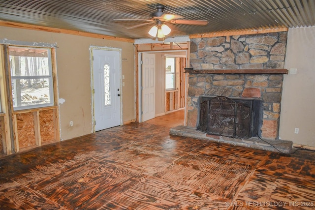 unfurnished living room with a stone fireplace, a wealth of natural light, and a ceiling fan
