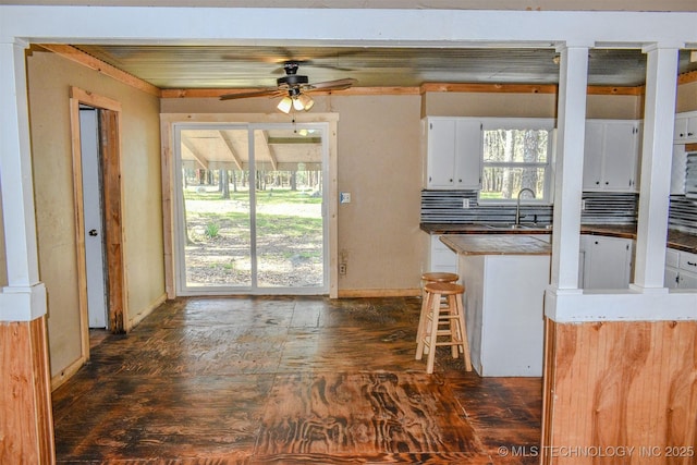 kitchen featuring white cabinetry, baseboards, a breakfast bar, a sink, and ceiling fan