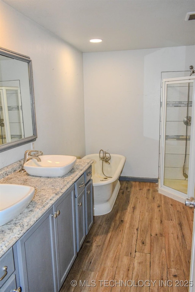 full bathroom featuring a shower stall, a soaking tub, a sink, double vanity, and wood finished floors