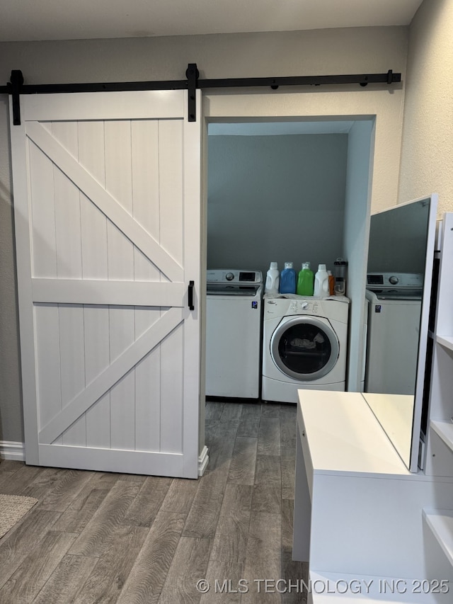 clothes washing area with washing machine and dryer, dark wood-type flooring, and a barn door