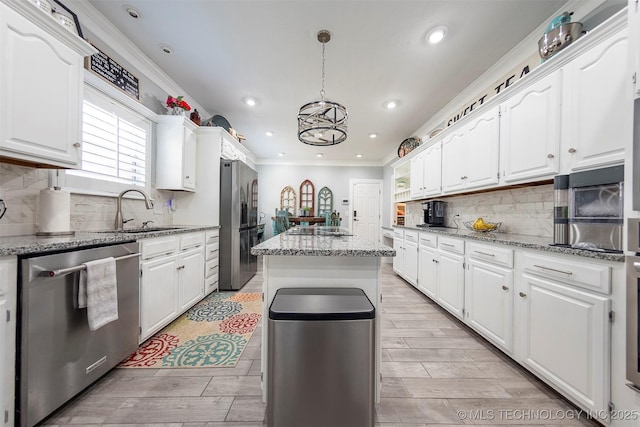 kitchen with appliances with stainless steel finishes, sink, a center island, white cabinetry, and pendant lighting