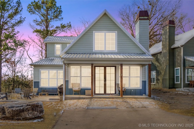 back of property at dusk featuring covered porch, a chimney, metal roof, and board and batten siding