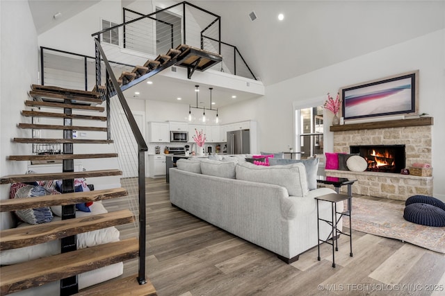 living area featuring stairs, a fireplace, high vaulted ceiling, and wood finished floors