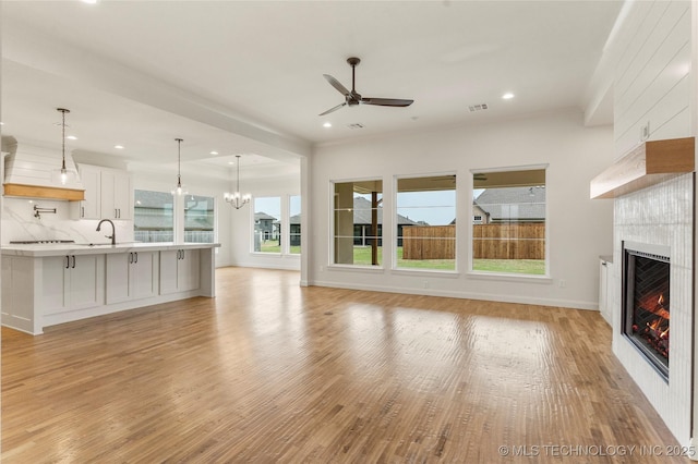 2982 E 145th St S, Bixby, OK 74008 - unfurnished living room featuring baseboards, recessed lighting, light wood-style floors, ceiling fan with notable chandelier, and a fireplace