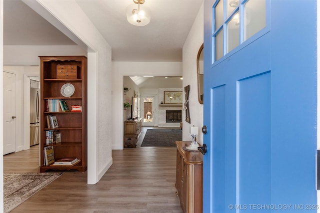 foyer entrance featuring baseboards, wood finished floors, and a fireplace