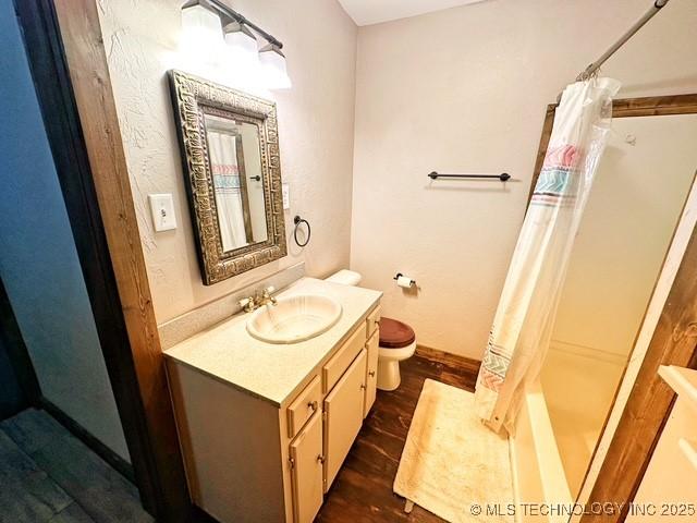 bathroom with shower / tub combo, baseboards, toilet, wood finished floors, and vanity