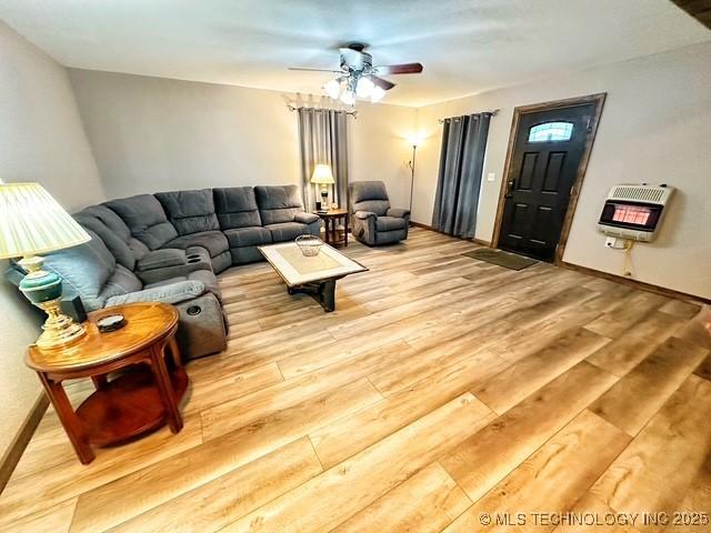 living area featuring heating unit, a ceiling fan, baseboards, and wood finished floors