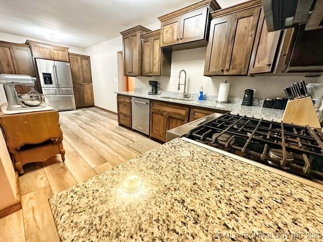 kitchen with stainless steel appliances, light stone counters, light wood-type flooring, and a sink