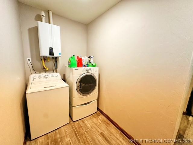 laundry area featuring tankless water heater, laundry area, wood finish floors, baseboards, and washing machine and clothes dryer