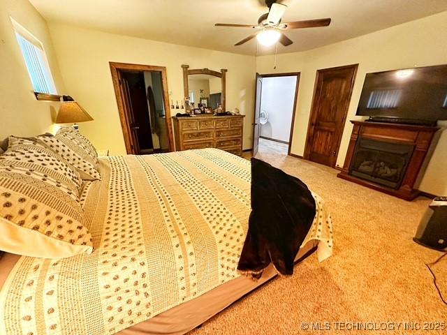 bedroom with light carpet, ceiling fan, and a glass covered fireplace