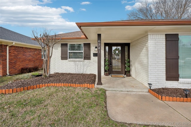 entrance to property with a yard, roof with shingles, and brick siding