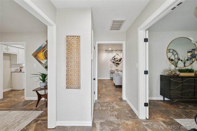 hallway featuring stone finish flooring, visible vents, and baseboards