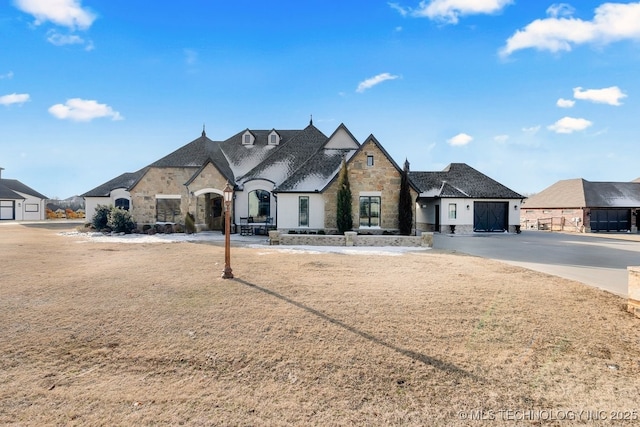 french country inspired facade with stone siding, a residential view, and concrete driveway