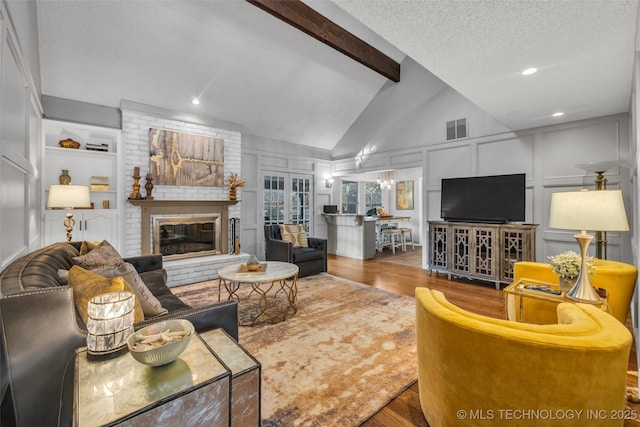 living area with a textured ceiling, a decorative wall, wood finished floors, visible vents, and beamed ceiling