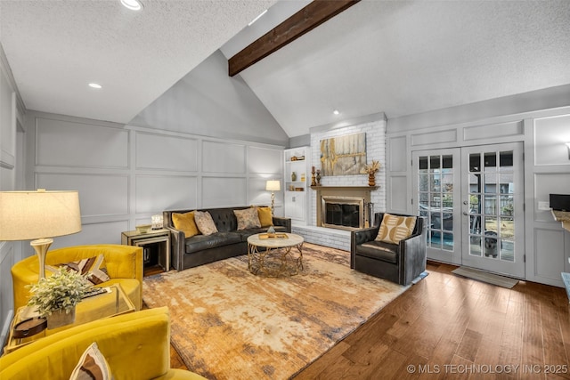 living room featuring a textured ceiling, lofted ceiling with beams, a decorative wall, a fireplace, and wood finished floors