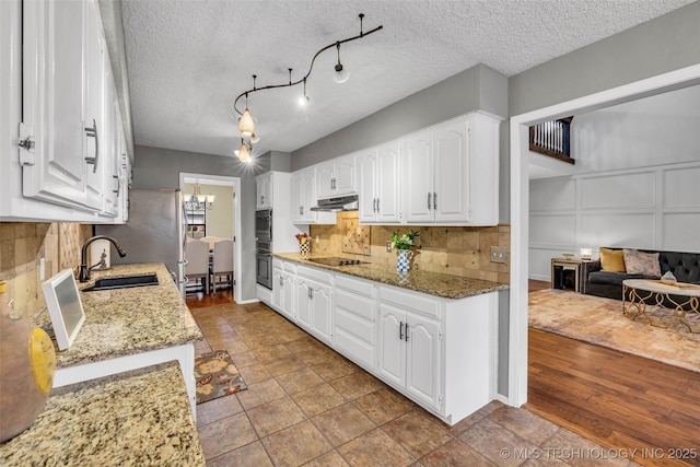 kitchen featuring stone counters, under cabinet range hood, white cabinets, and a sink