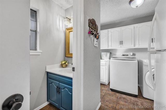 clothes washing area featuring cabinet space, baseboards, a textured ceiling, washer and dryer, and a sink