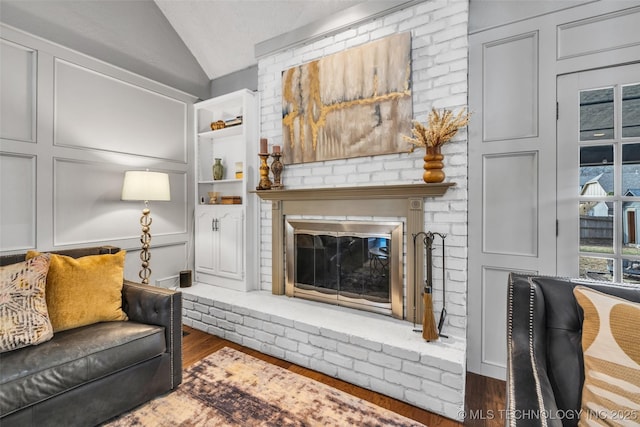 living room featuring lofted ceiling, dark wood-style floors, a fireplace, and a decorative wall