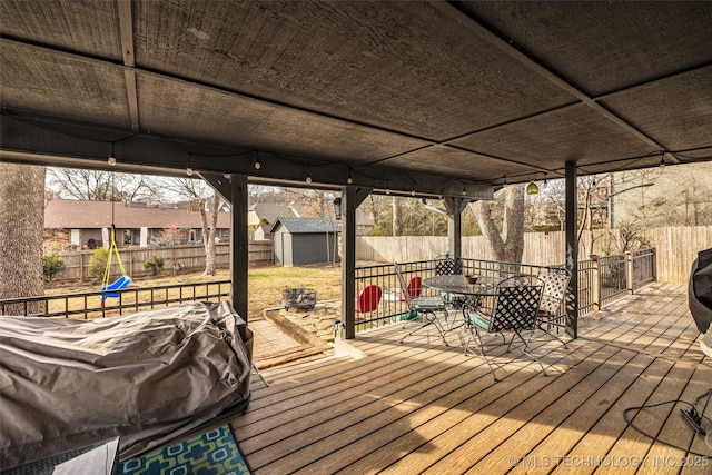 wooden terrace featuring a storage shed, a fenced backyard, outdoor dining area, an outdoor structure, and a playground