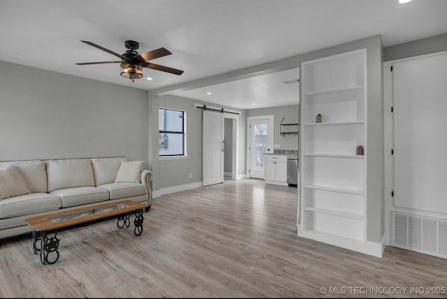 living room with ceiling fan, a barn door, and light hardwood / wood-style flooring