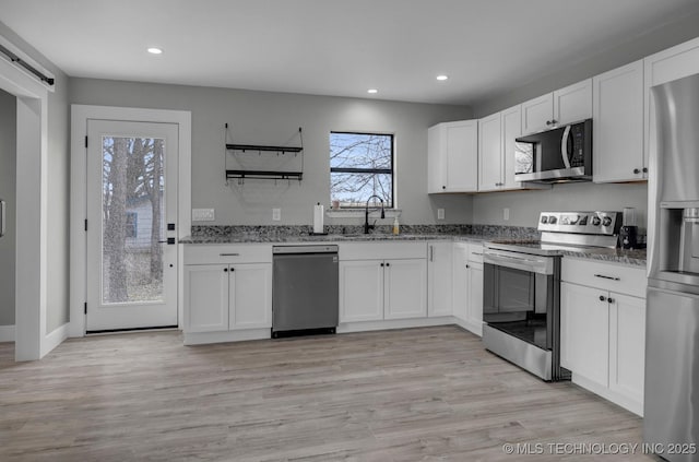 kitchen featuring sink, stone countertops, stainless steel appliances, a barn door, and white cabinets