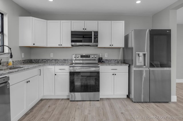 kitchen featuring white cabinetry, stainless steel appliances, light stone counters, and sink