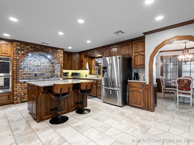 kitchen with light stone counters, a notable chandelier, a kitchen island, crown molding, and stainless steel appliances