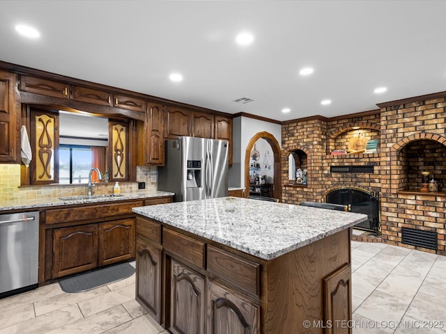 kitchen with appliances with stainless steel finishes, decorative backsplash, a kitchen island, sink, and a brick fireplace