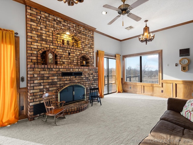 living room with carpet floors, ornamental molding, a fireplace, and ceiling fan with notable chandelier